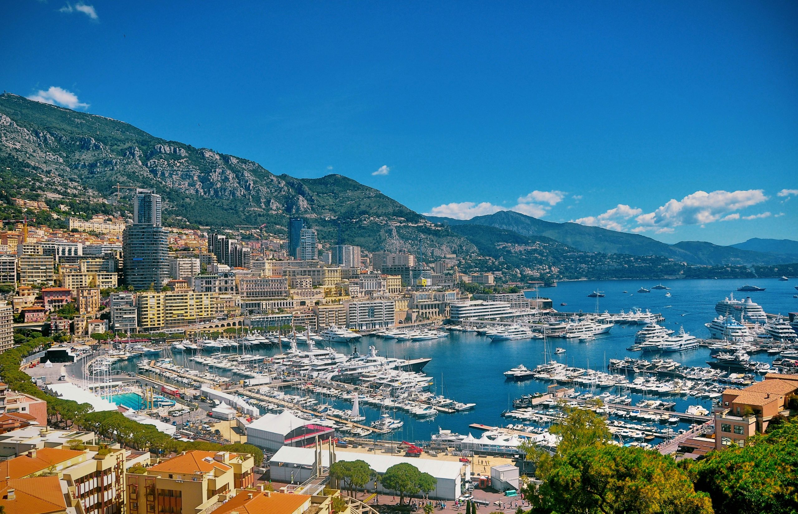 A view of Port Hercule and the Monaco skyline, illustrating the density of prestige real estate in Monaco. The harbor is filled with luxury superyachts, bordered by the Stade Nautique Rainier III, while the backdrop features high-rise residential architecture nestled against the steep Maritime Alps. The image captures the essence of the Principality’s world-class maritime infrastructure and its status as a premier global real estate destination.